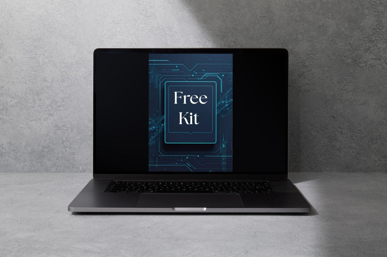 A dark gray laptop sits open on a light gray surface against a textured gray wall, with the screen displaying a blue graphic that reads 'Free Kit'.
