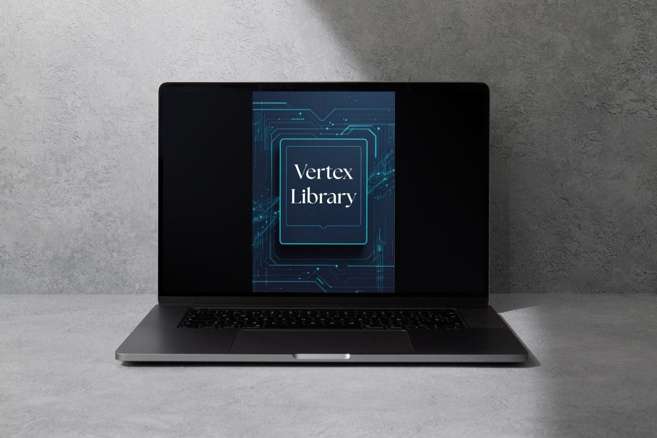 A dark gray laptop sits open on a light gray surface against a textured gray wall, with the screen displaying a blue and black graphic labeled 'Vertex Library'.
